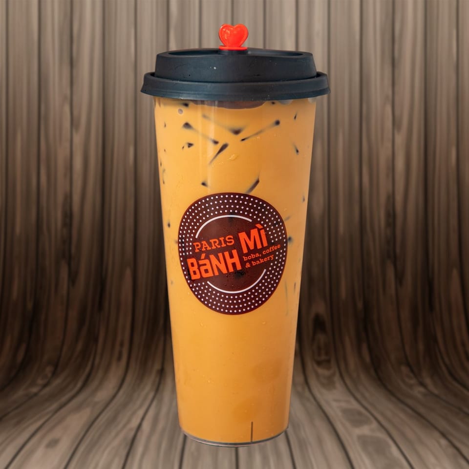 Iced Thai tea with boba in a clear cup with a black lid and red heart stopper.