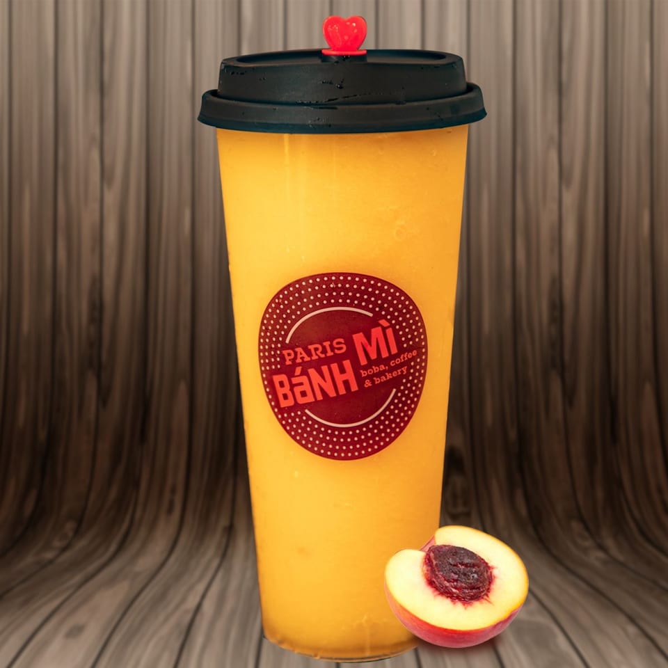 A Paris Banh Mi peach smoothie with a heart-shaped straw stopper and a peach half.
