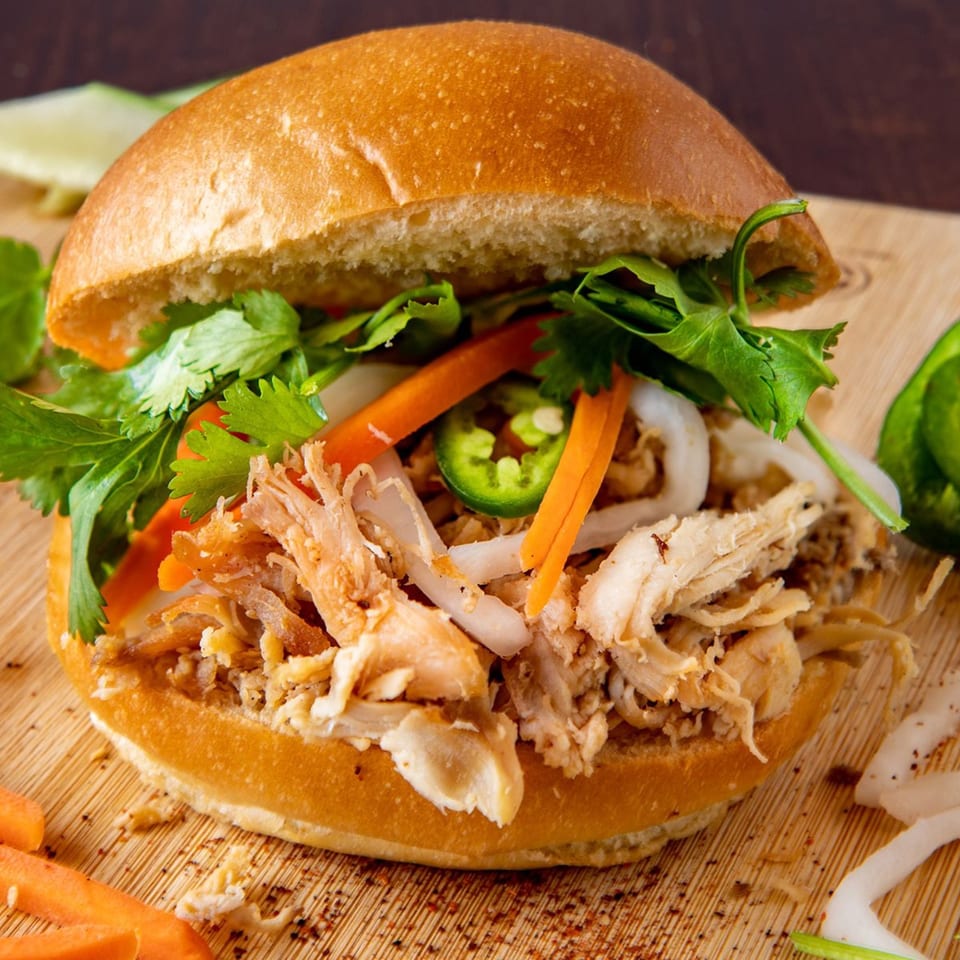 A close-up of a Paris Banh Mi sandwich filled with shredded chicken, carrots, onions, cilantro, and jalapeños.