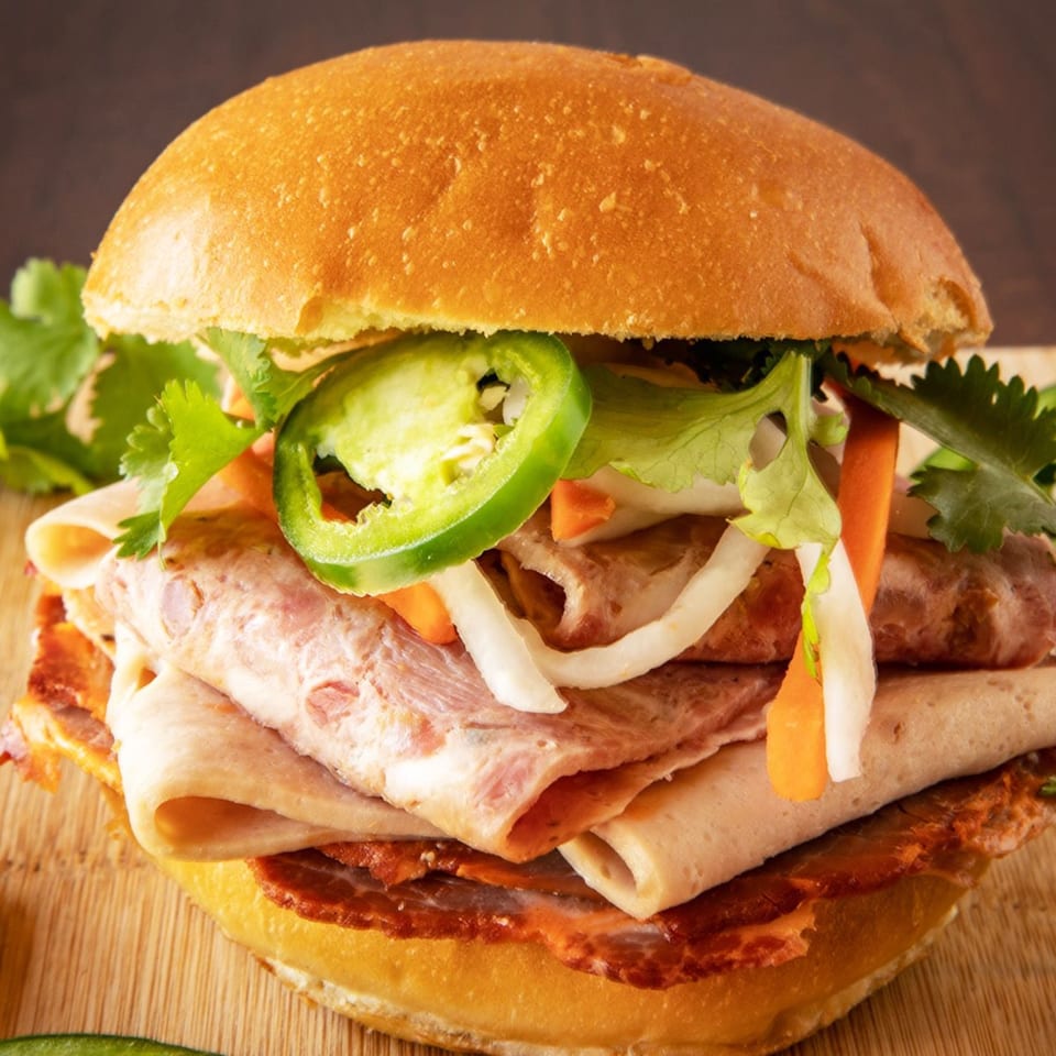 A Vietnamese banh mi sandwich with various meats, pickled vegetables, cilantro, and jalapeños on a bun.