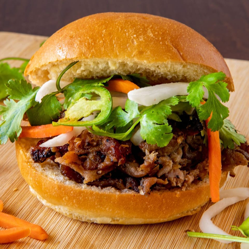A Vietnamese banh mi sandwich with meat, cilantro, jalapeños, onions, and carrots on a wooden board.