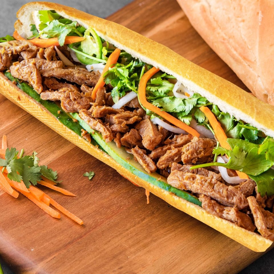 A Vietnamese banh mi sandwich, filled with meat, cilantro, carrots, and onions, on a wooden board.