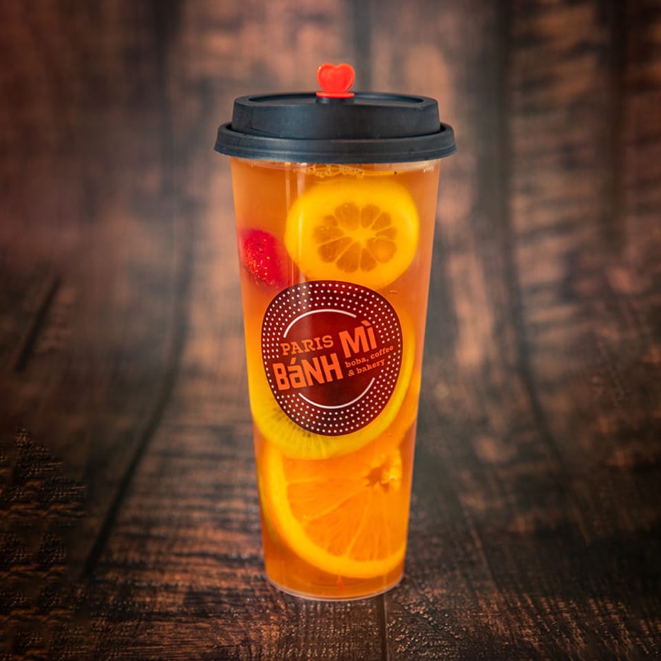 Paris Banh Mi fruit tea with orange, kiwi, and strawberry slices, on a wooden surface.